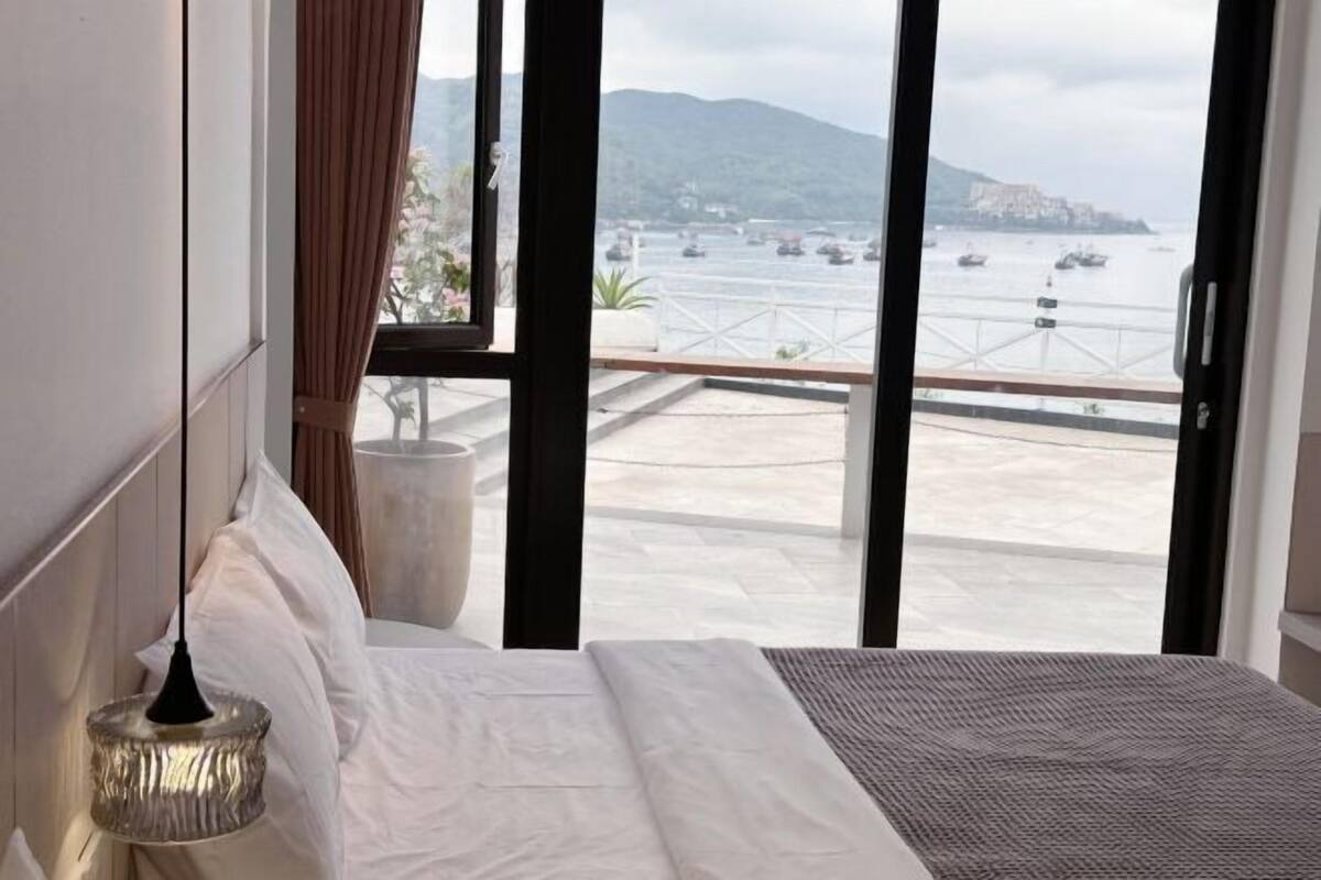 Een hotelkamer met een groot bed, uitzicht op zee en een balkon met een hekwerk.
