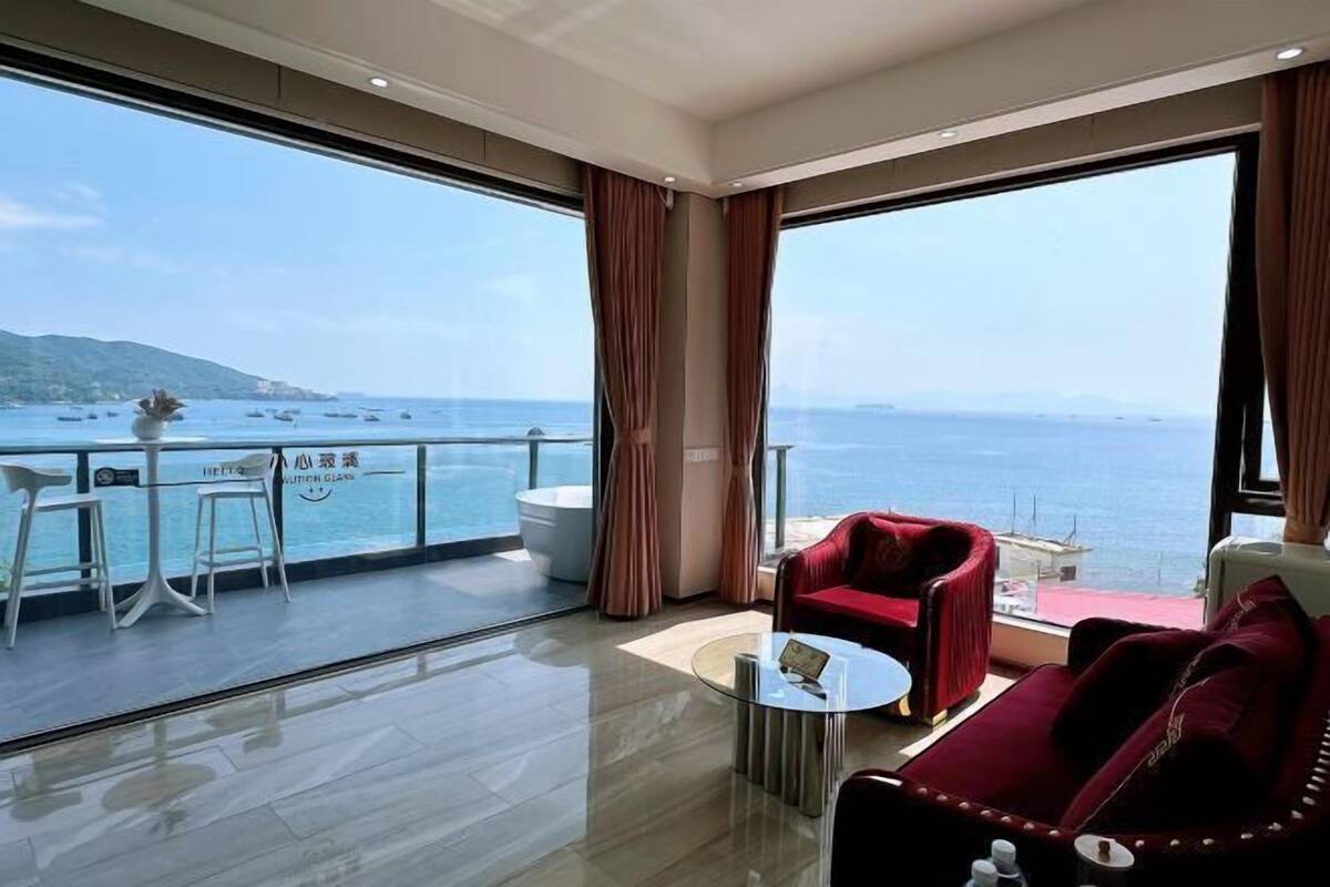 Een moderne hotelkamer met een ruim balkon, een rode bank, een klein rond tafeltje en uitzicht op zee.