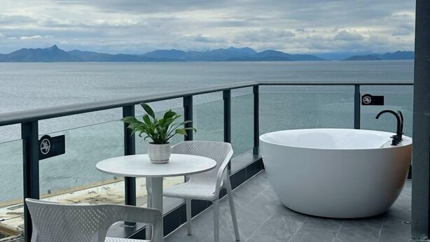 Un balcon avec une baignoire blanche, une table ronde agrémentée d’une plante en pot et une chaise.