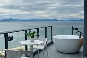 A balcony with a white bathtub, a round table with a potted plant, and a chair. - Yougan Xiaozhu Seaview Hostel (Shenzhen)