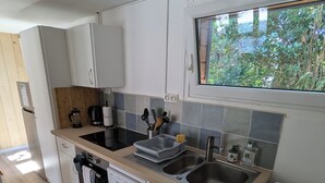 A compact kitchen with white cabinets, a wooden countertop, a built-in dishwasher, and a window with a view of greenery.