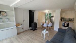 A modern living room with a grey sofa, a dining table with chairs, a kitchen area with appliances, and a white door leading to another room.