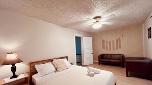 A bedroom with a bed, a nightstand, a lamp, a ceiling fan, a sofa, and a chair.
