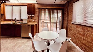 A compact kitchen with a dishwasher, wooden cabinets, and a window with blinds.