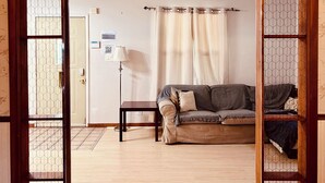 A room with a wooden floor, a sofa, a table, and a lamp. There is a door with a mesh screen and a wall-mounted sign.