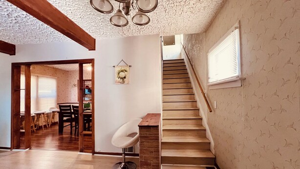 A spacious living area with a staircase, a dining area in the background, and a modern chair.