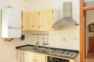 Una cocina con armarios de madera clara, un refrigerador blanco, un lavamanos de acero inoxidable y una estufa a gas.