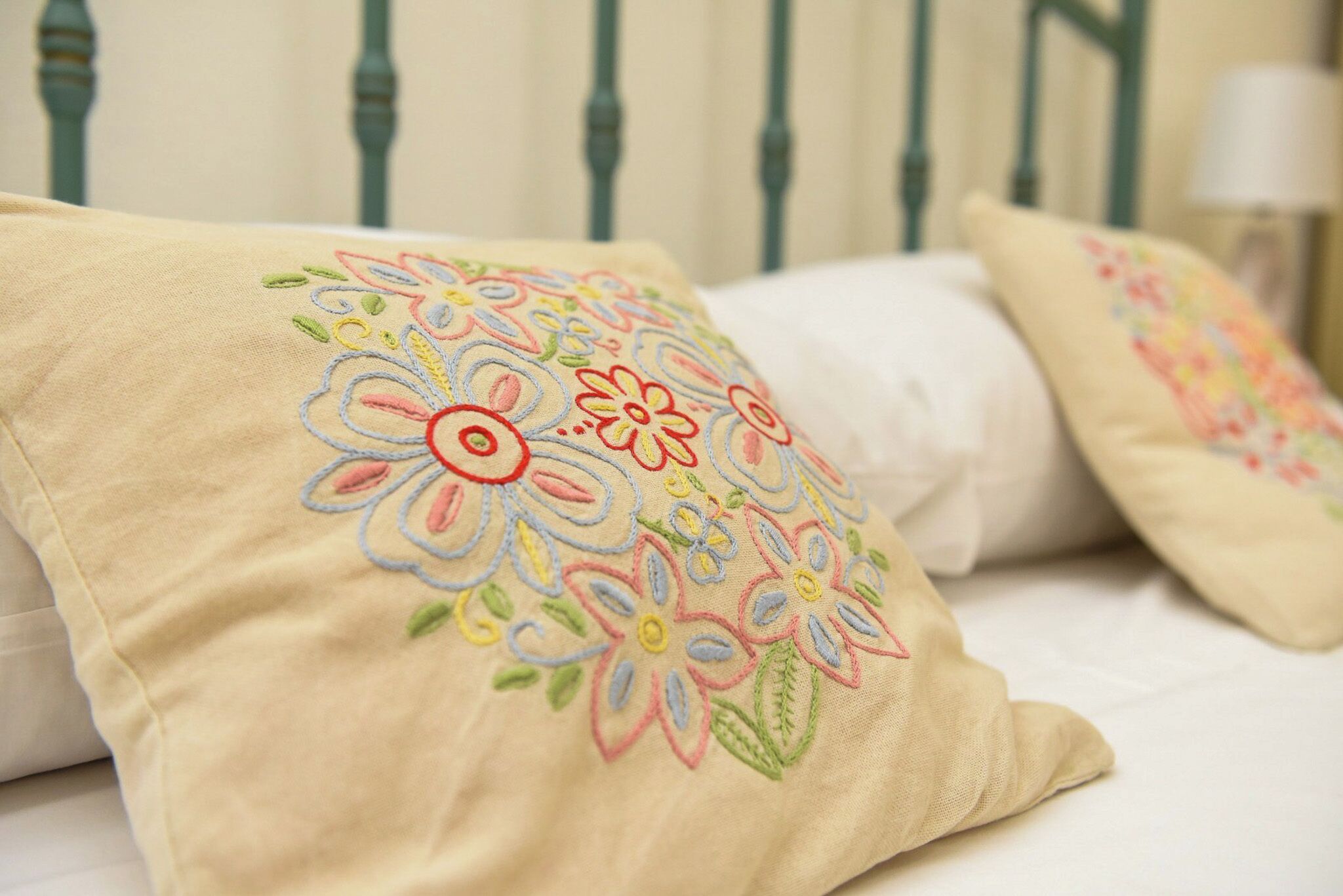 A bed with beige pillows featuring colorful floral embroidery.