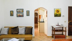 A living room with a sofa, a coffee table, and a small table with a vase. There are framed pictures on the wall and a door to the right. - Casa Isabella (Nuoro)