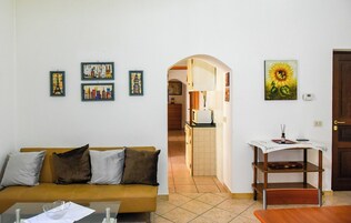 Una sala de estar con un sofá, una mesa de centro y una mesita con un jarrón. Se observan cuadros enmarcados en la pared y una puerta a la derecha.