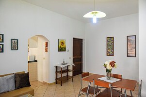 A dining area with a table and chairs, a vase with flowers, and a wall with framed pictures.