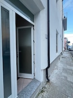 Un edificio residencial con puerta corredera de vidrio, un pequeño escalón exterior y el número '8' visible en la pared.