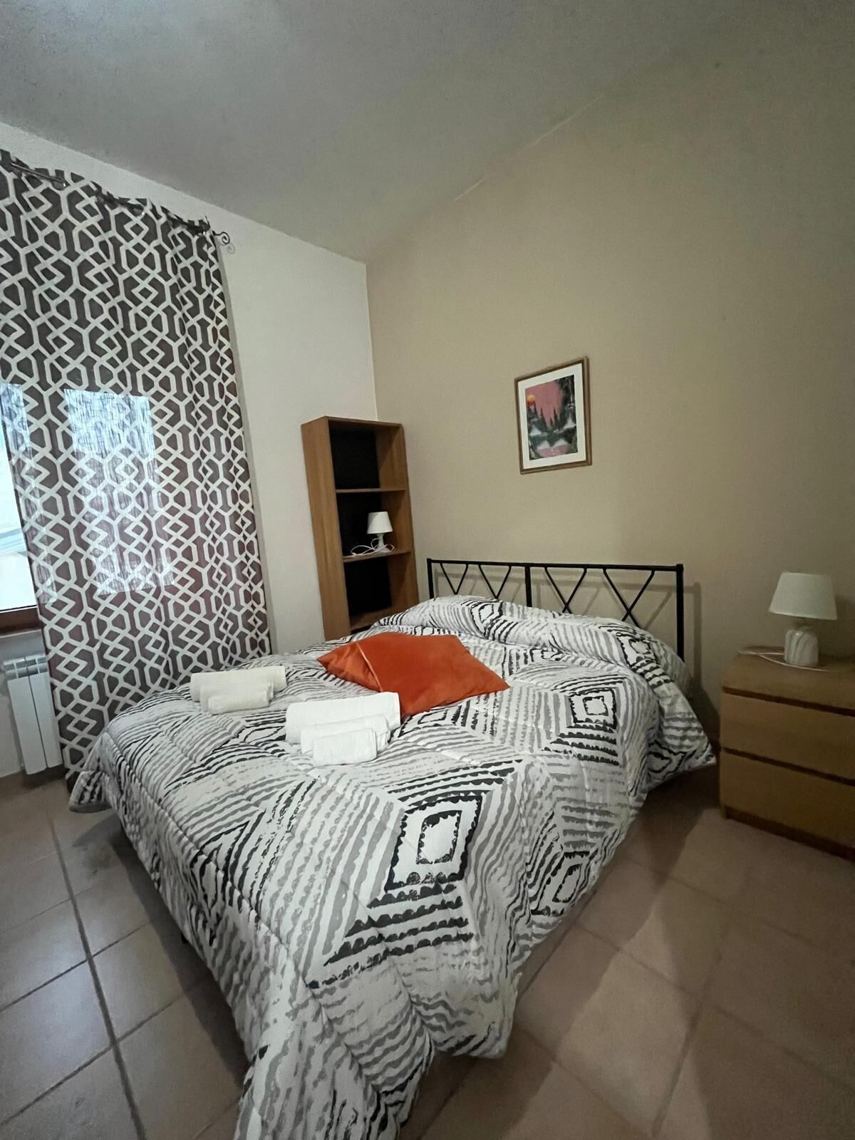 A neatly made bed with patterned bedding, a bedside table with a lamp, and a decorative wall piece.