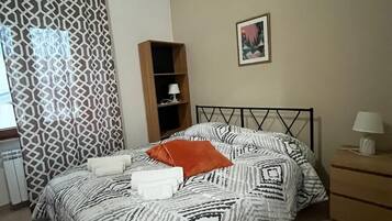 A neatly made bed with patterned bedding, a bedside table with a lamp, and a decorative wall piece.