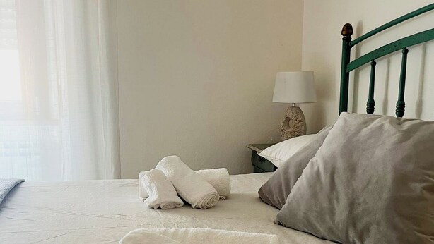 A neatly made bed with rolled towels, a pillow, and a bedside lamp on a nightstand. - Casa Isabella (Nuoro)