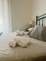 Una cama bien hecha con toallas enrolladas, una almohada y una lámpara de noche en una mesita.