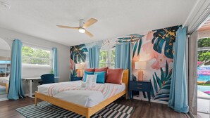 A modern bedroom with a wooden bed, a ceiling fan, a desk, and a large window with curtains.