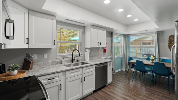 A modern kitchen with white cabinets, a black stove, and a dining area with blue chairs and a wooden table.