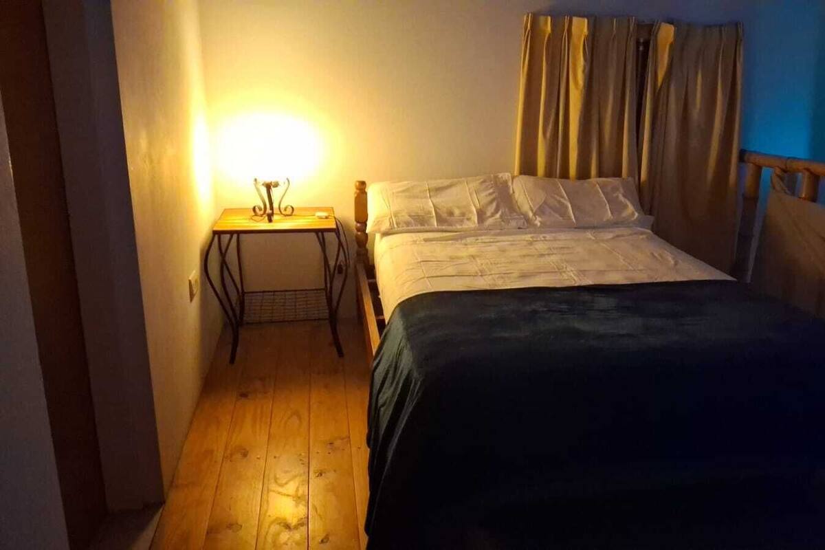 Ein Schlafzimmer mit einem Bett, einem Nachttisch, einer Lampe und einem Fenster mit Vorhängen.