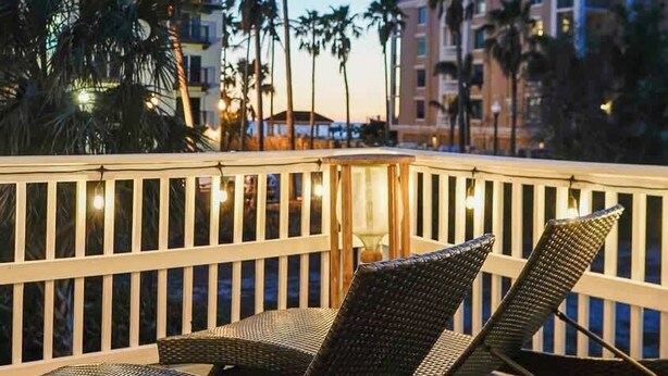 Un balcone con poltrone in vimini, un pontile in legno e vista su palme e edifici.