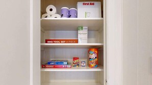 Uno scaffale bianco con diversi oggetti, tra cui un kit di pronto soccorso, carta igienica e giochi da tavolo.