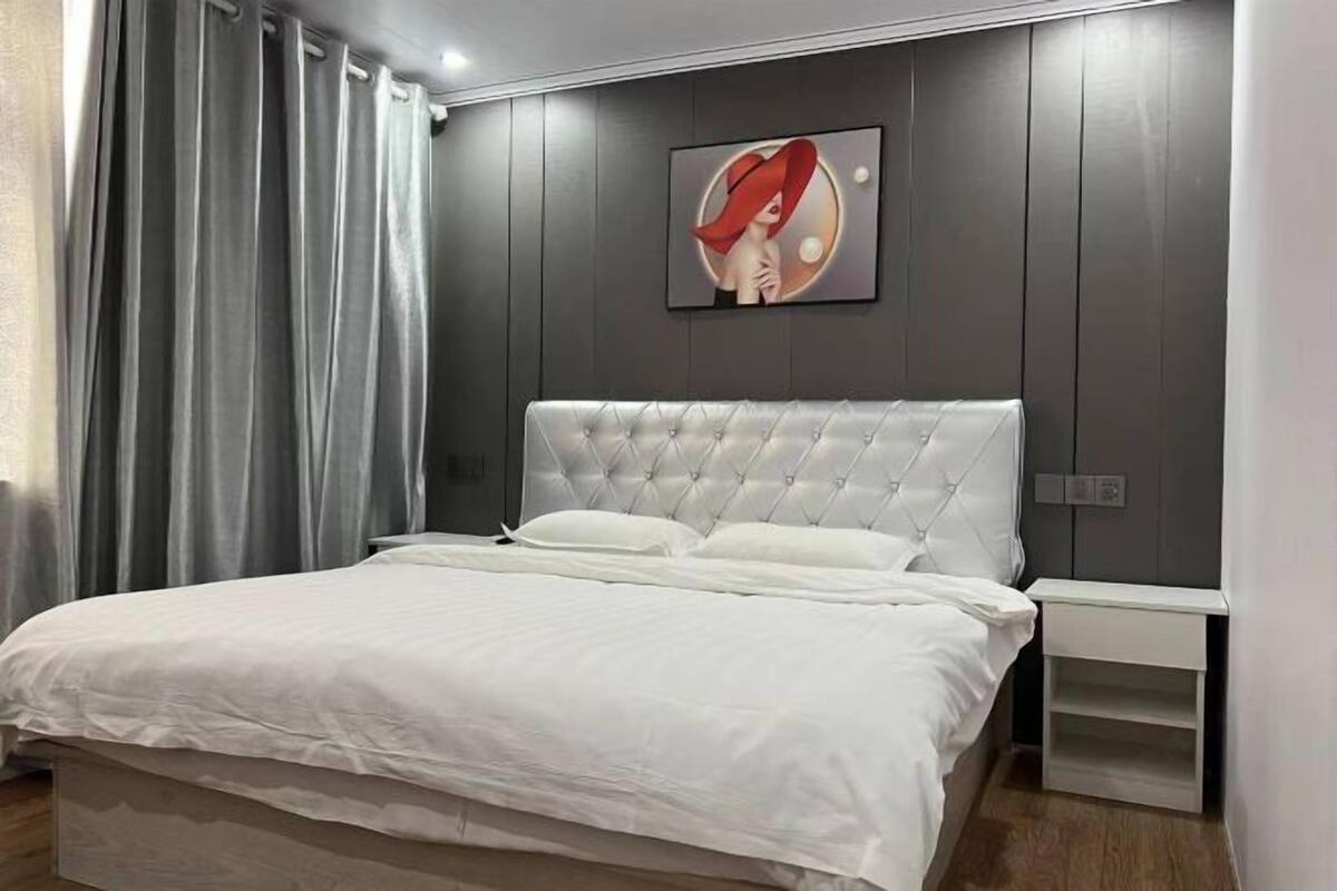 A modern bedroom with a tufted headboard, a white bedspread, and a nightstand with a drawer.