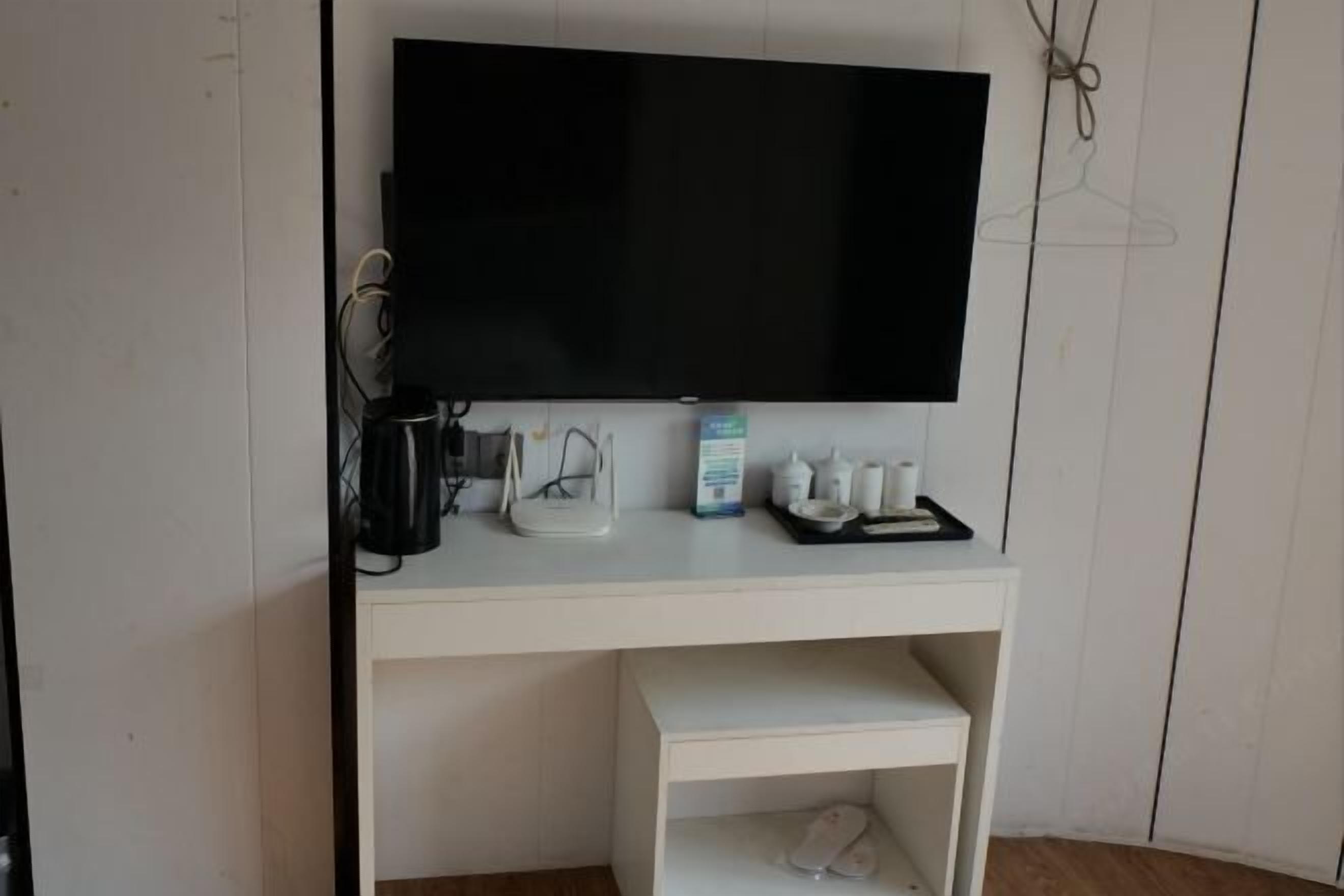 A white desk with a flat-screen TV, a coffee maker, and a small shelf below.