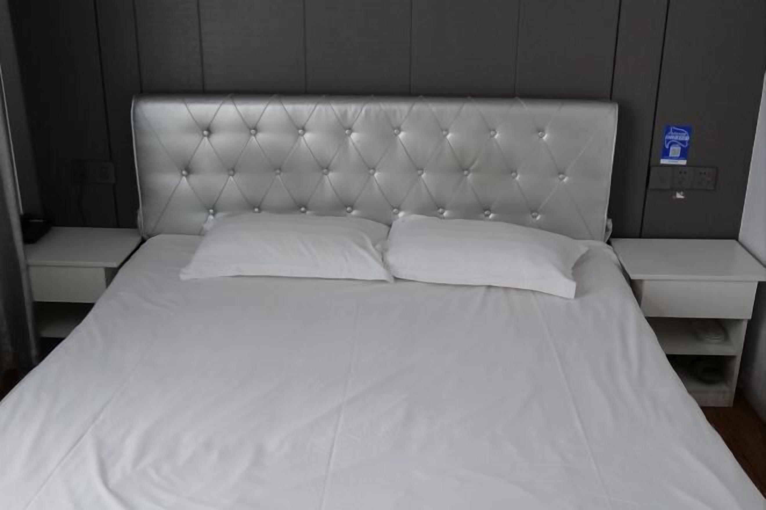 A bed with a tufted headboard, two pillows, and a white bedspread.