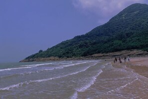 A beach with waves, a sandy shore, and a hill with greenery. - Lianyungang Pearl Hotel (Lianyungang)