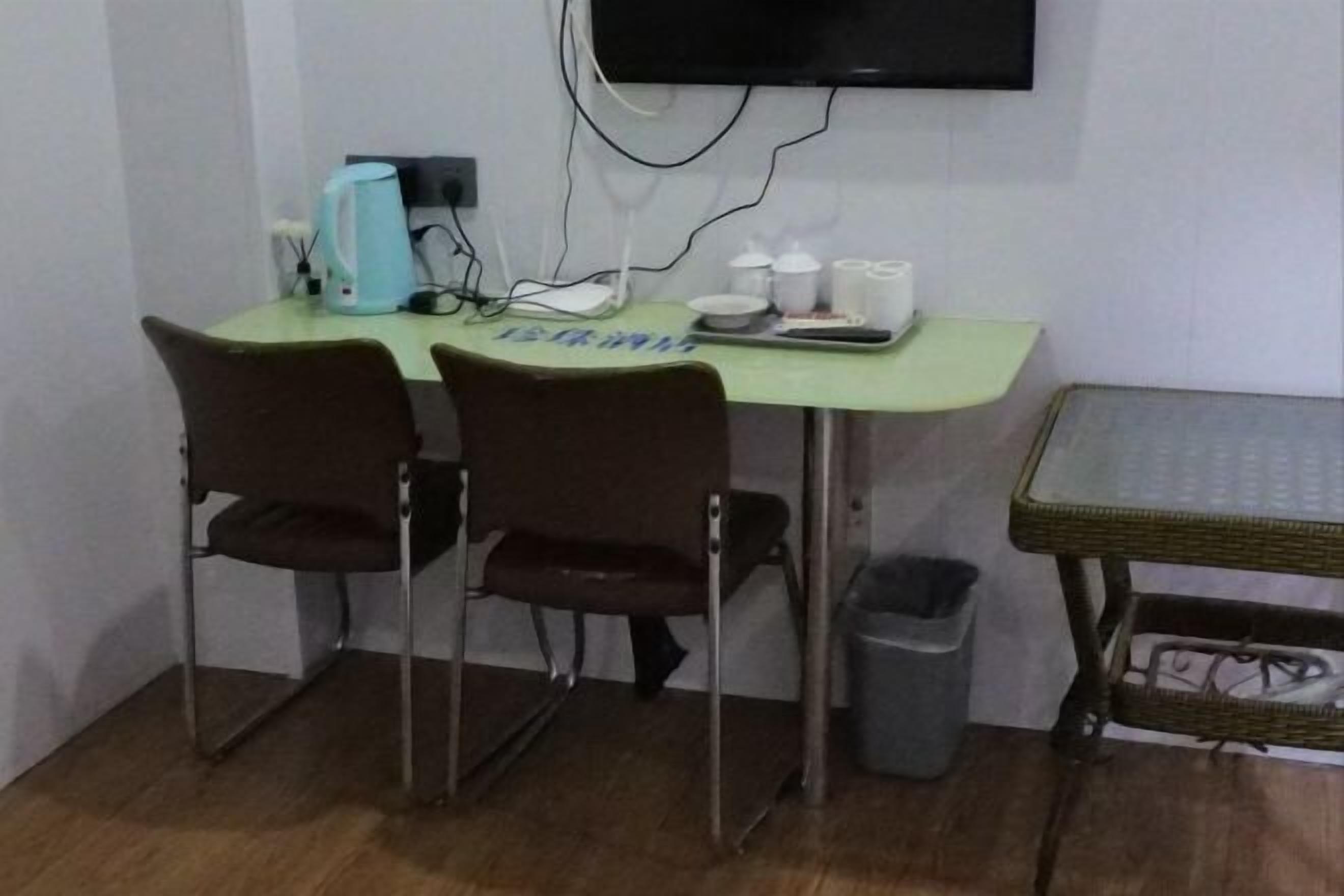 A small room with a desk, two chairs, a television mounted on the wall, and a trash bin.
