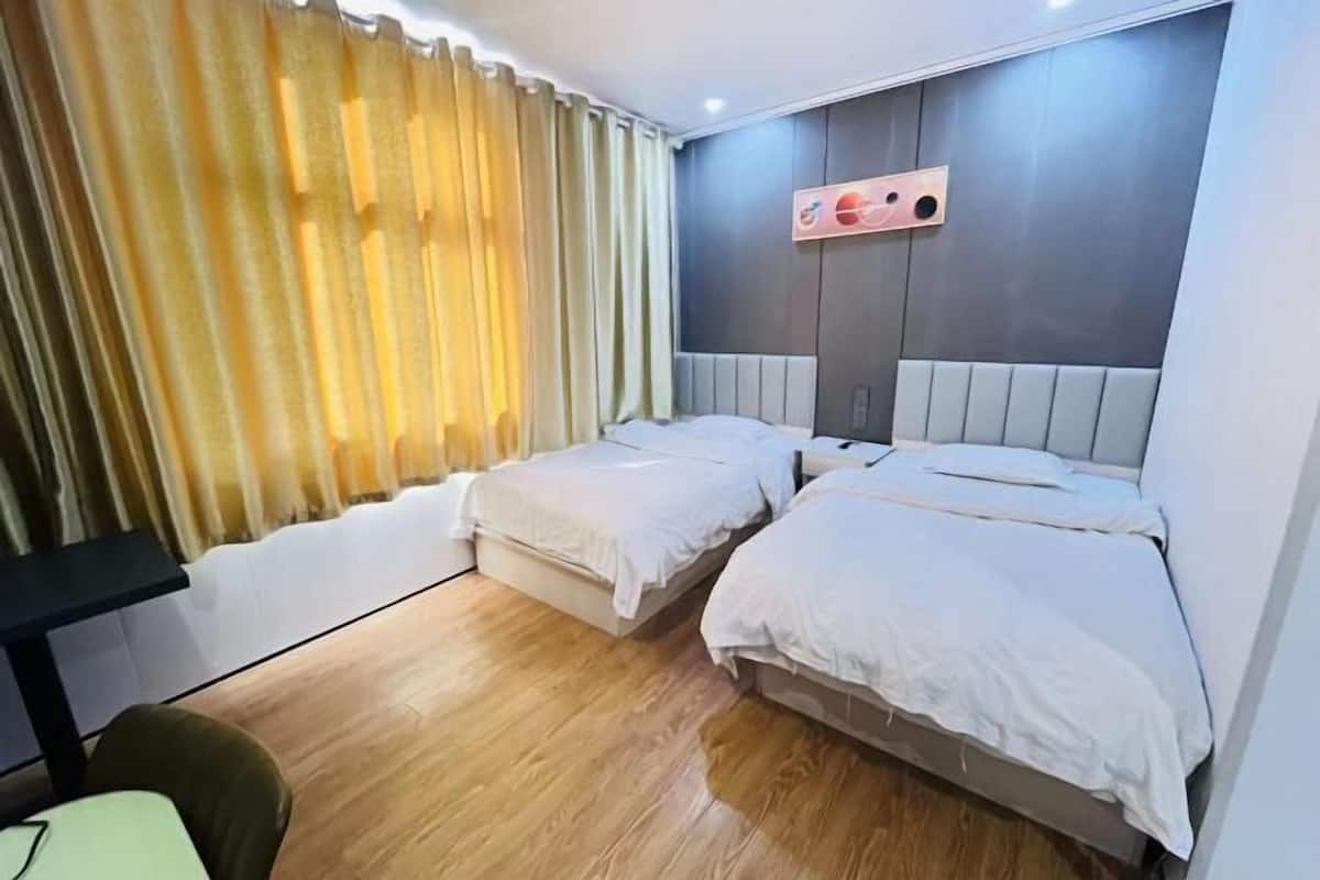 A hotel room with two beds, a desk, and a window with curtains.