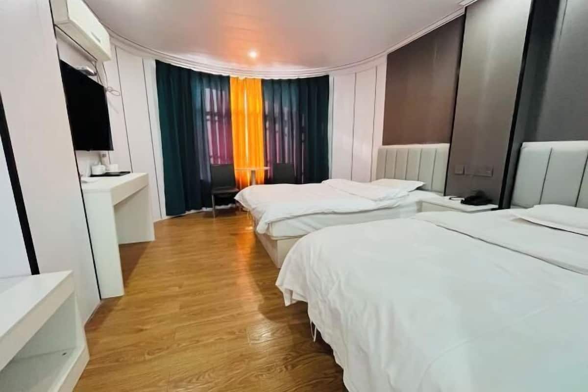 A hotel room with two beds, a desk, a chair, and a window with curtains.