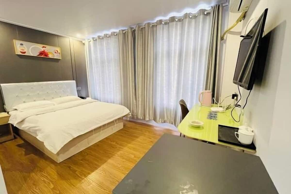 A hotel room with a bed, a desk, a chair, a TV, and a window with curtains.