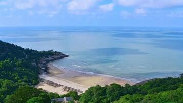 A coastal landscape with a beach, clear sky, and dense greenery.
