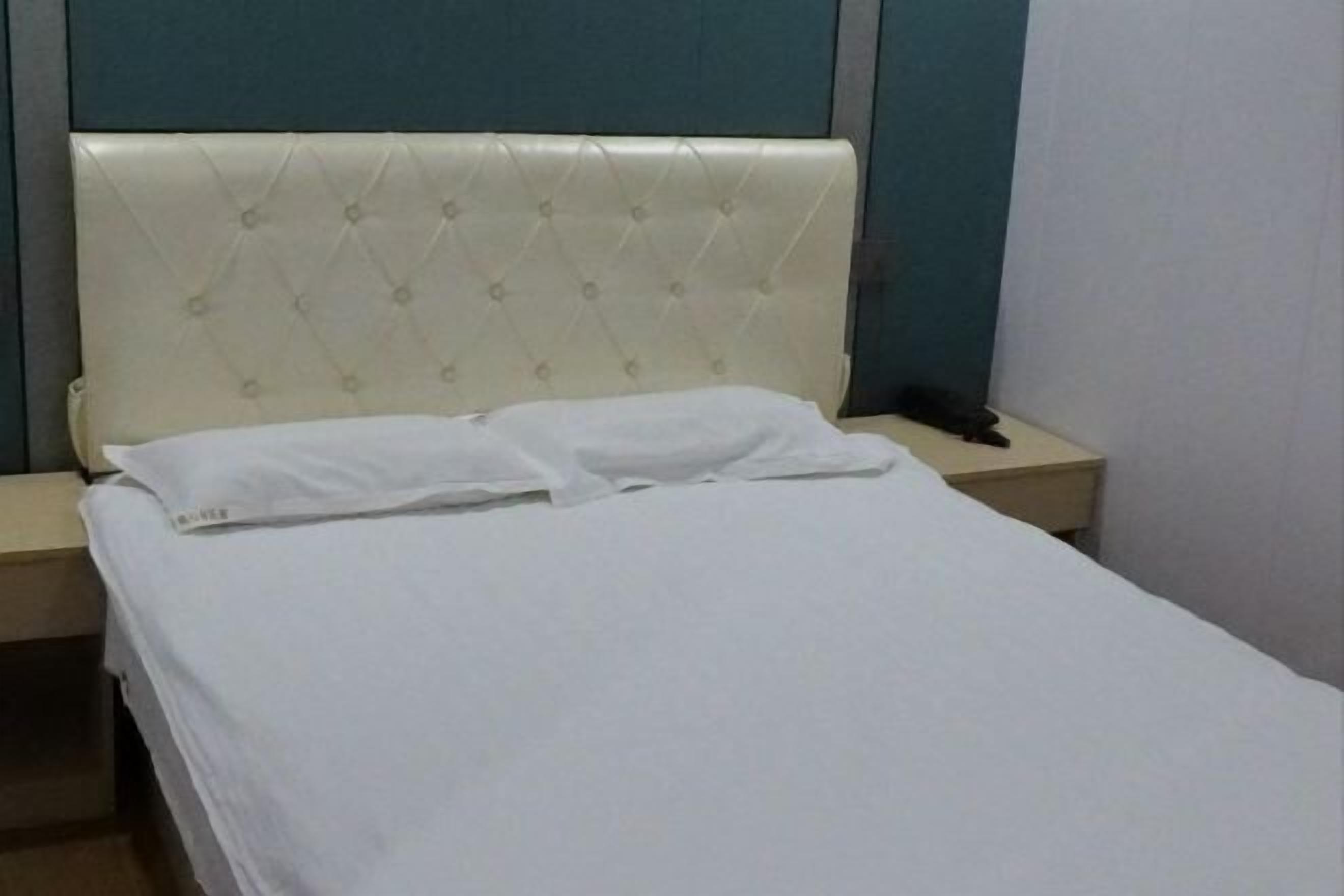 A bed with a tufted headboard, a bedside table, and a wall-mounted telephone.