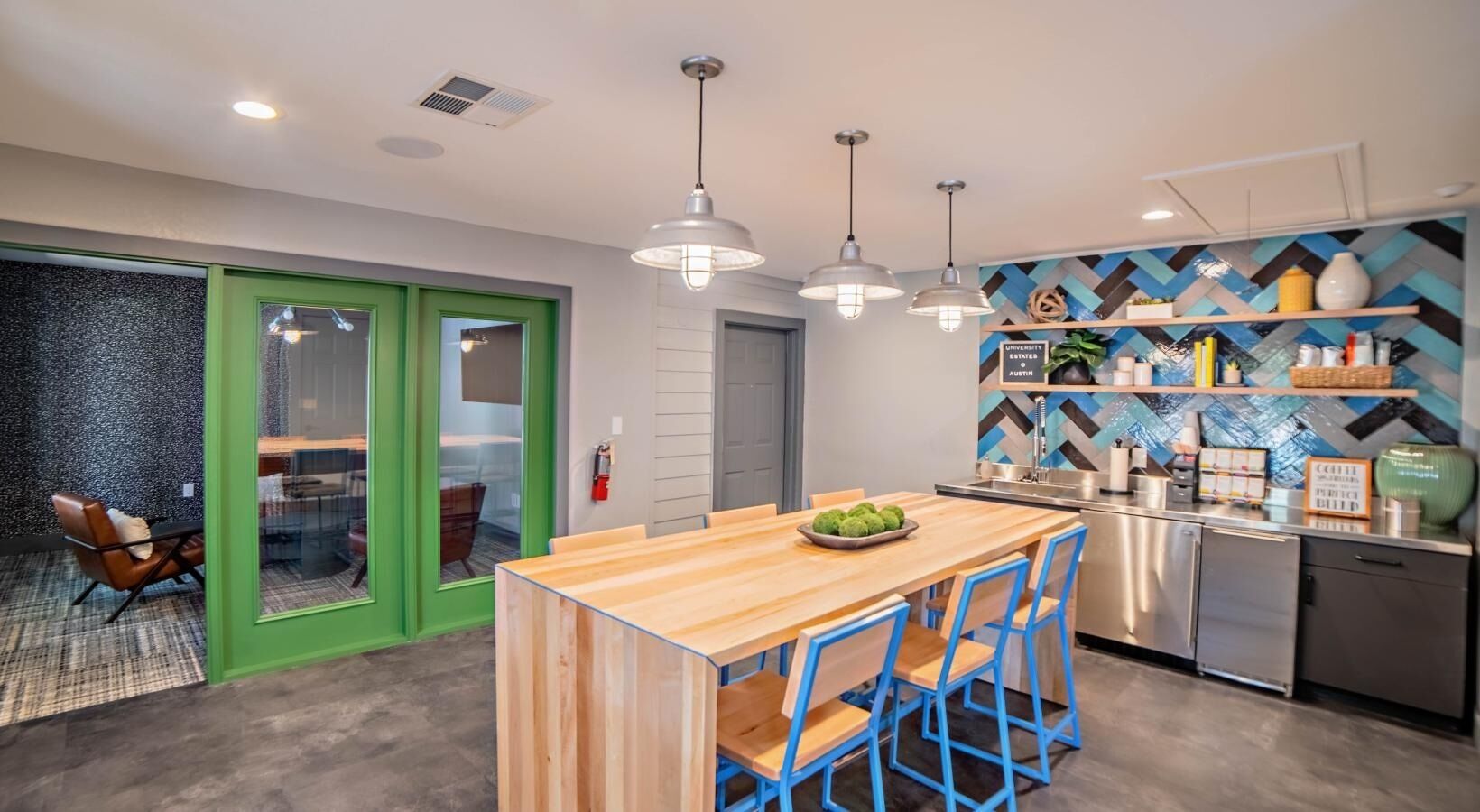 Une cuisine moderne avec un îlot central en bois, des chaises bleues et un dosseret orné d’un motif en chevrons.