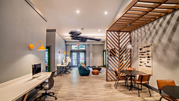 A modern office space with a long table, chairs, and a sofa. There are desks with computers and a TV. - Homey Modern 3BR Retreat w/Resort Pool (Austin)