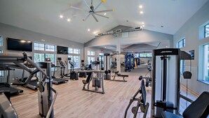 A spacious gym with various exercise equipment, large windows, and a high ceiling with a central light fixture. - Homey Modern 3BR Retreat w/Resort Pool (Austin)