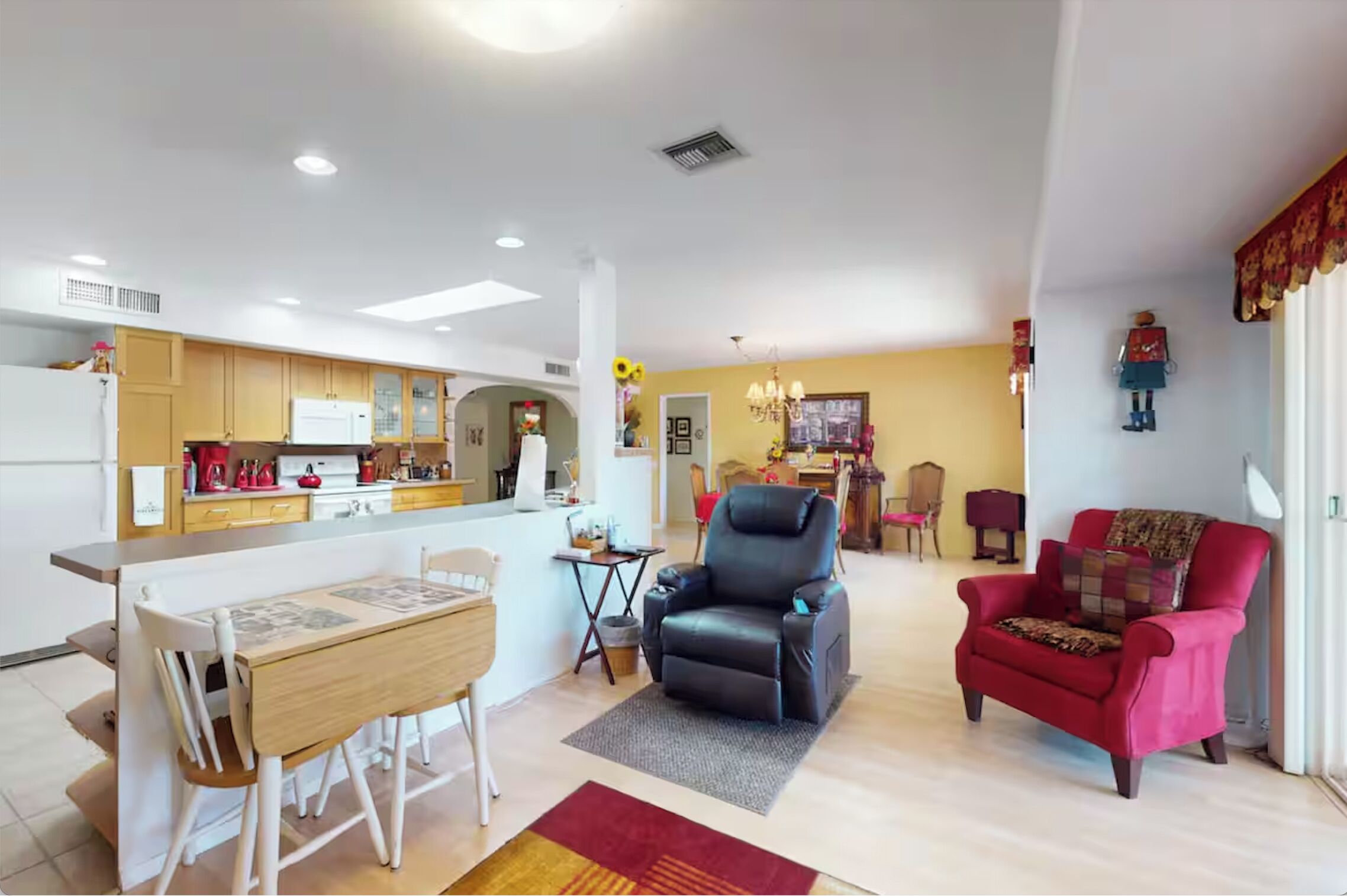 A spacious living area with a dining table, a black leather chair, and a red armchair.