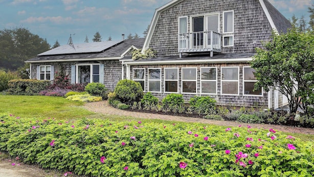 A two-story house with a large balcony, surrounded by a well-maintained garden with flowering plants. - Bay Views: Peaceful Acadia National Park Getaway! (Steuben)