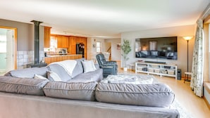 A modern living room with a grey sectional sofa, a flat-screen TV, and a kitchen in the background. - Bay Views: Peaceful Acadia National Park Getaway! (Steuben)