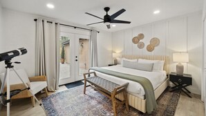 A bedroom with a bed, a desk, a telescope, and a ceiling fan.