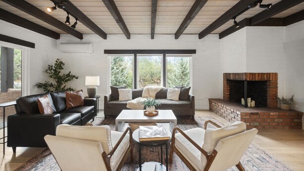 A spacious living room with a fireplace, a black leather sofa, a white armchair, and a coffee table.