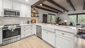 A modern kitchen with white cabinetry, stainless steel appliances, and a wooden ceiling.
