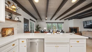 A modern kitchen with white cabinetry, a stainless steel dishwasher, and a large island with a gold faucet.