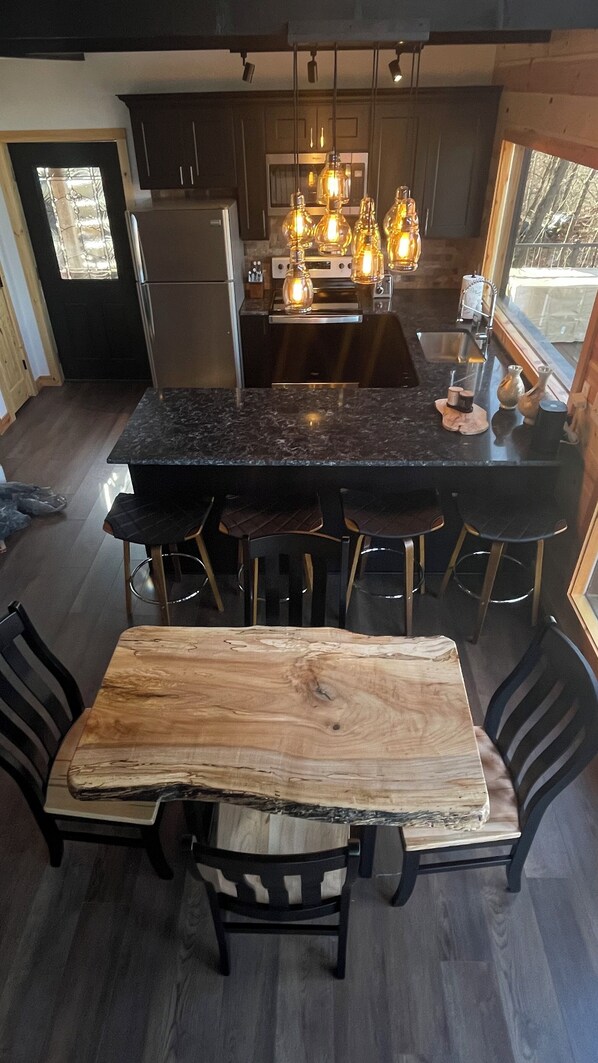 Een moderne keuken met een centraal kookeiland, barstoelen en een eettafel met stoelen.