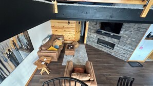 Un salon moderne avec un canapé, un fauteuil et une petite table. On y trouve une cheminée et un plafond en bois.
