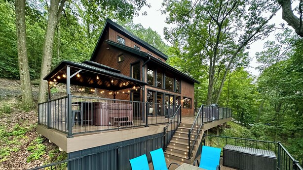 Une cabane moderne en bois, dotée d’une terrasse, d’un espace salon extérieur et d’une cheminée.