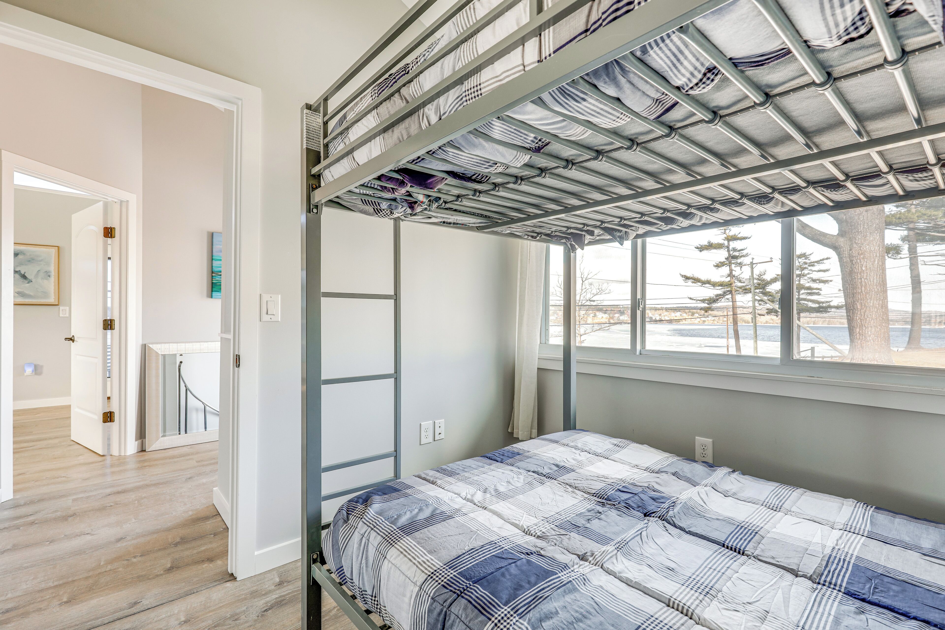 Ein Schlafzimmer mit Etagenbett, einem Fenster mit Blick auf Bäume und einer Tür zu einem anderen Raum.