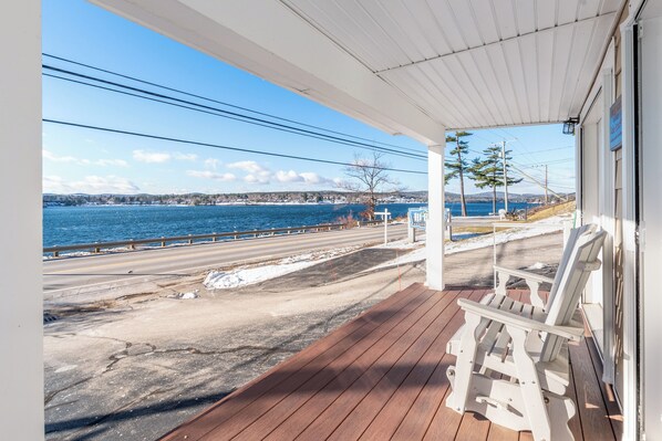 A wooden deck with a view of a coastal road and a body of water. - Steps to Beach: Lake-View Laconia Getaway! (Laconia)